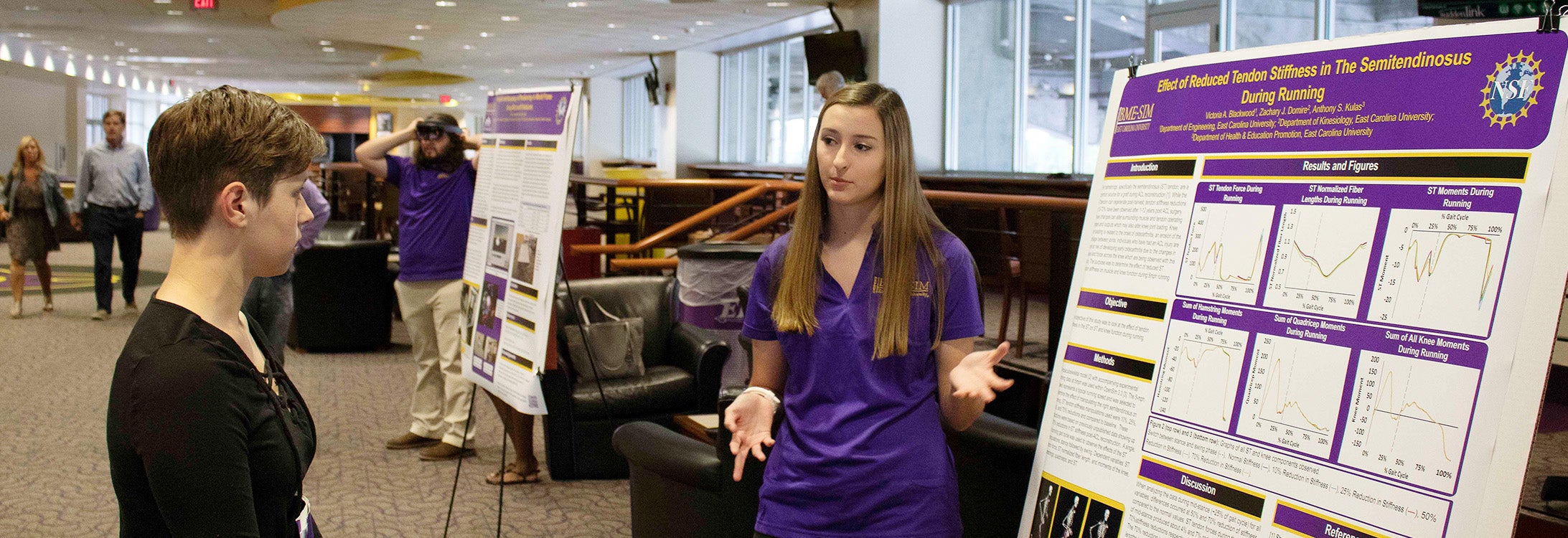 Rising East Carolina University junior Victoria Blackwood, right, shares her research on osteoarthritis in patients who have undergone ACL surgery at the The Biomedical Engineering in Simulations, Imaging and Modeling Research Experience for Undergraduates post session at Dowdy-Ficklen Stadium on Friday.